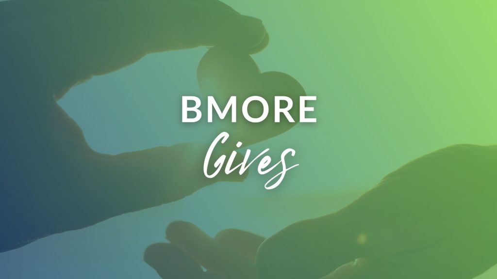 Hands forming a heart shape with the text "B'More Gives" prominently displayed in the center. Background features a gradient of blue and green.